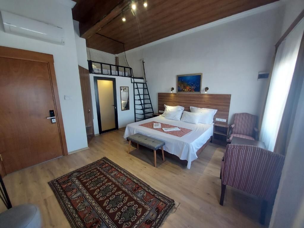 Quarto com cama, um banquinho, uma cadeira, uma escada e um quadro na parede.
