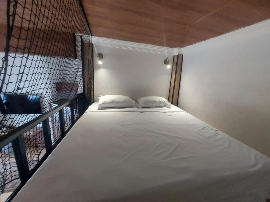 A single bed with white bedding in a room with a wooden ceiling and white walls.
