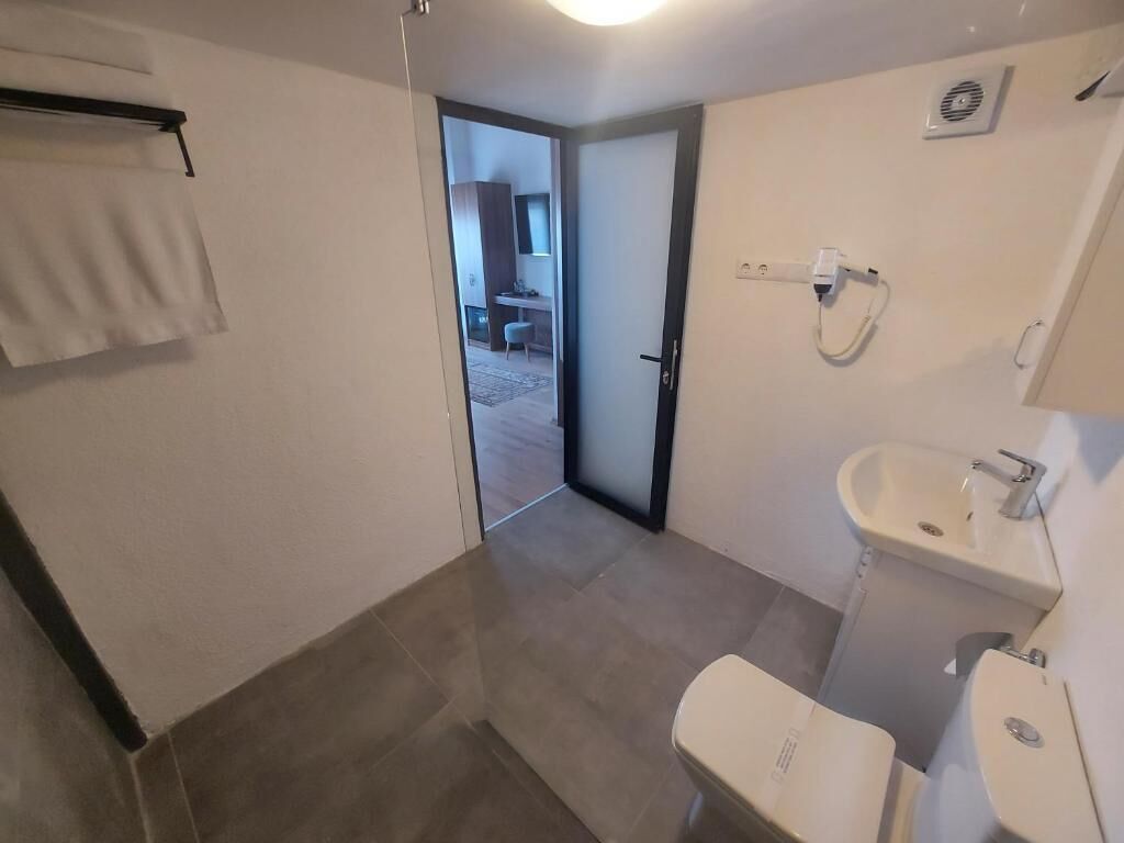 A bathroom with a toilet, sink, and shower. There is a towel rack and a door leading to a hallway.