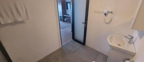 A bathroom with a toilet, sink, and shower. There is a towel rack and a door leading to a hallway.