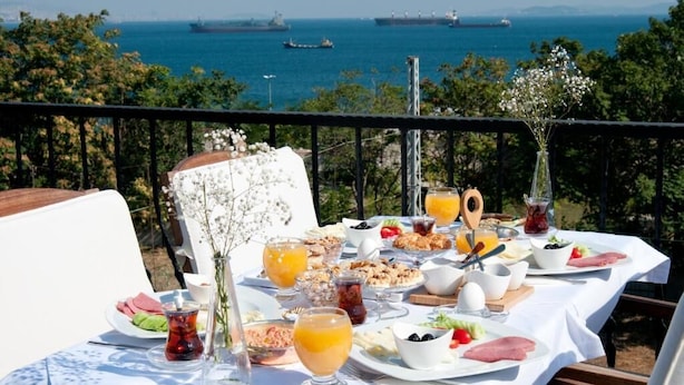 A table set with breakfast items and drinks, overlooking a scenic coastal view with ships in the distance. - Queen Seagull Boutique Hotel (İstanbul)