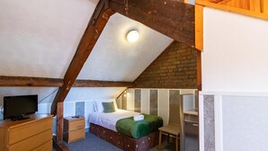 A small, cozy bedroom with a sloped ceiling, a single bed, a wooden dresser, a television, and a small table. - Standard Twin Room - Shared (Newcastle upon Tyne)
