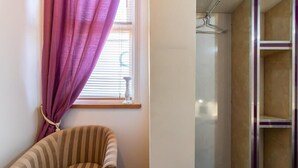 A striped armchair, a window with purple curtains, and a shower area with a glass door. - OYO Bentleys Hotel Standard Single Room (Newcastle upon Tyne)