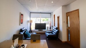 A modern living room with leather sofas, a flat-screen TV, and a large window offering a view of the street. - OYO Bentleys Hotel Standard Single Room (Newcastle upon Tyne)