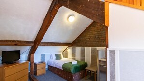 A bedroom with a sloped ceiling, a bed with a green bedspread, a wooden dresser, a television, and a small table. - OYO Bentleys Hotel Standard Single Room (Newcastle upon Tyne)