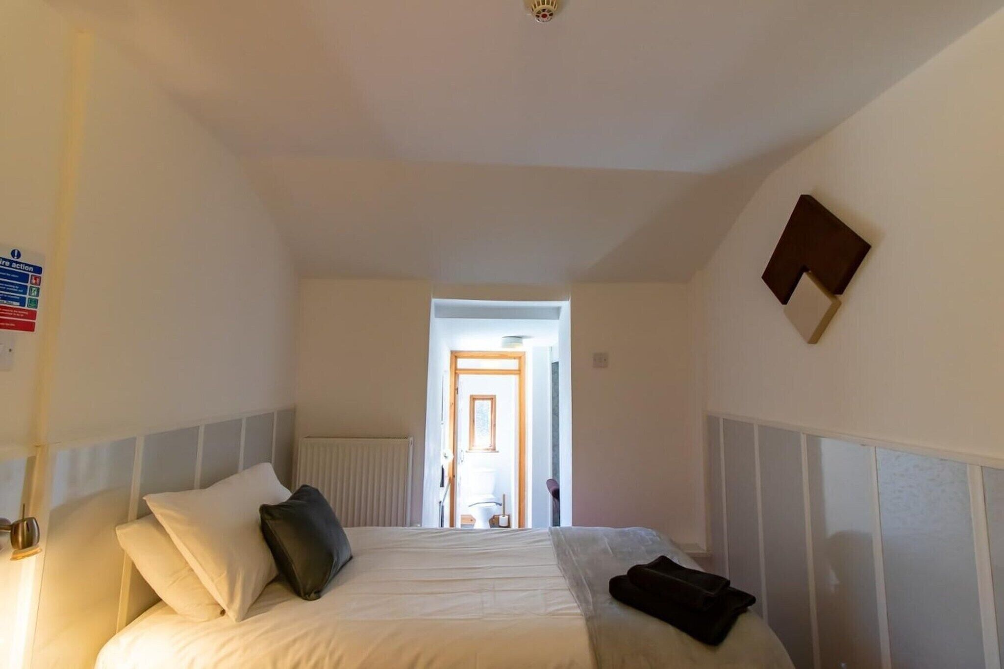 Una camera d'albergo con un letto, un comodino, una sveglia a parete e una porta che dà su un bagno.