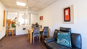 Un espace de vie compact comprenant un coin repas, une kitchenette et un canapé en cuir noir agrémenté d’un coussin à motifs.