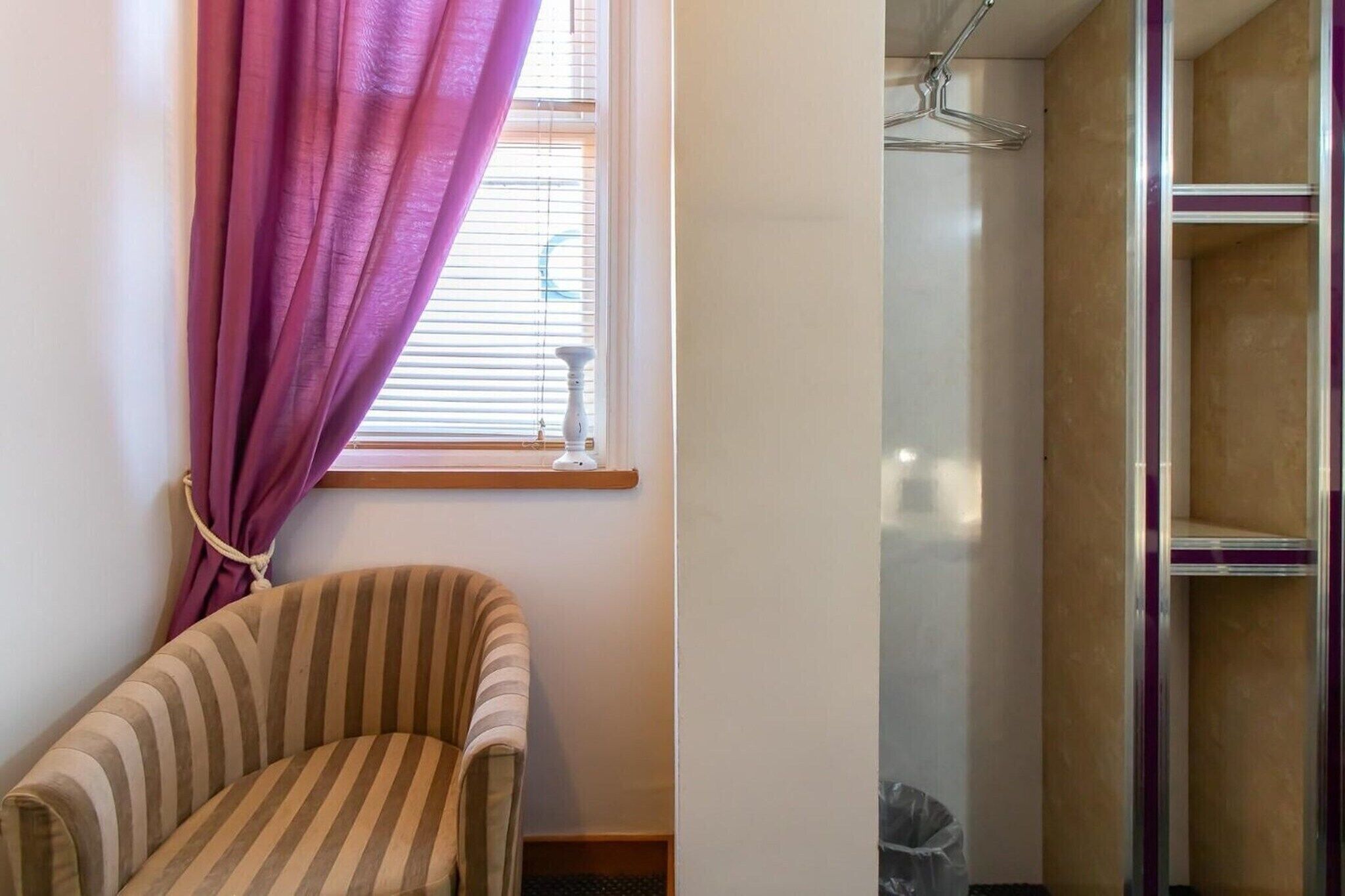 A striped armchair, a window with purple curtains, and a shower area with a glass door.