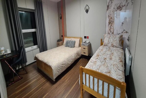 A bedroom with two beds, a desk, and a chair. - OYO Welsh Accomodation Standard Family of 3 Room (Pembroke Dock)