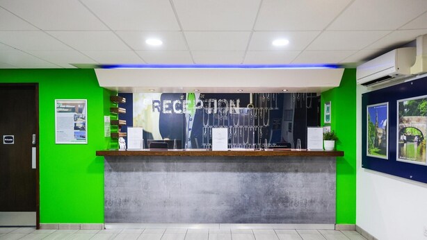 A reception area with a green wall, a reception desk, and a sign that reads "RECEPTION". - Standard Family of 3 Room (Lancaster)