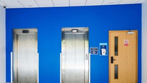 Two elevators and a door in a hallway with blue walls. - Standard Family of 3 Room (Lancaster)