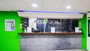 A reception desk with a green wall, a blue ceiling light, and a sign that reads "RECEPTION". - Standard Family of 3 Room (Lancaster)