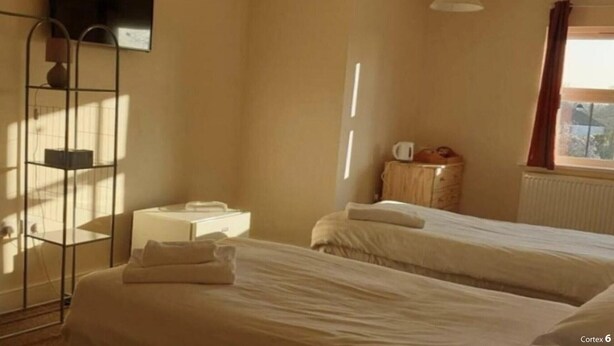 A bedroom with two beds, a bedside table, a lamp, and a window with curtains.