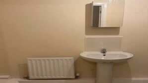 A bathroom with a white radiator, a pedestal sink, and a mirror above the sink. - Standard Double Room (Manchester)