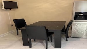A dining area with a black table and chairs, a flat-screen TV mounted on the wall, and a coffee machine. - Standard Double Room (Manchester)