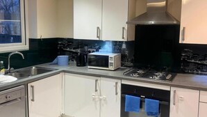 A modern kitchen with white cabinets, a stainless steel range hood, a microwave, and a gas stove. - Standard Double Room (Manchester)