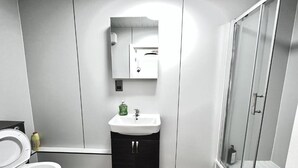 A modern bathroom with a white sink, dark cabinets, a glass shower enclosure, and a toilet. - Standard Double Studio (Pembroke Dock)