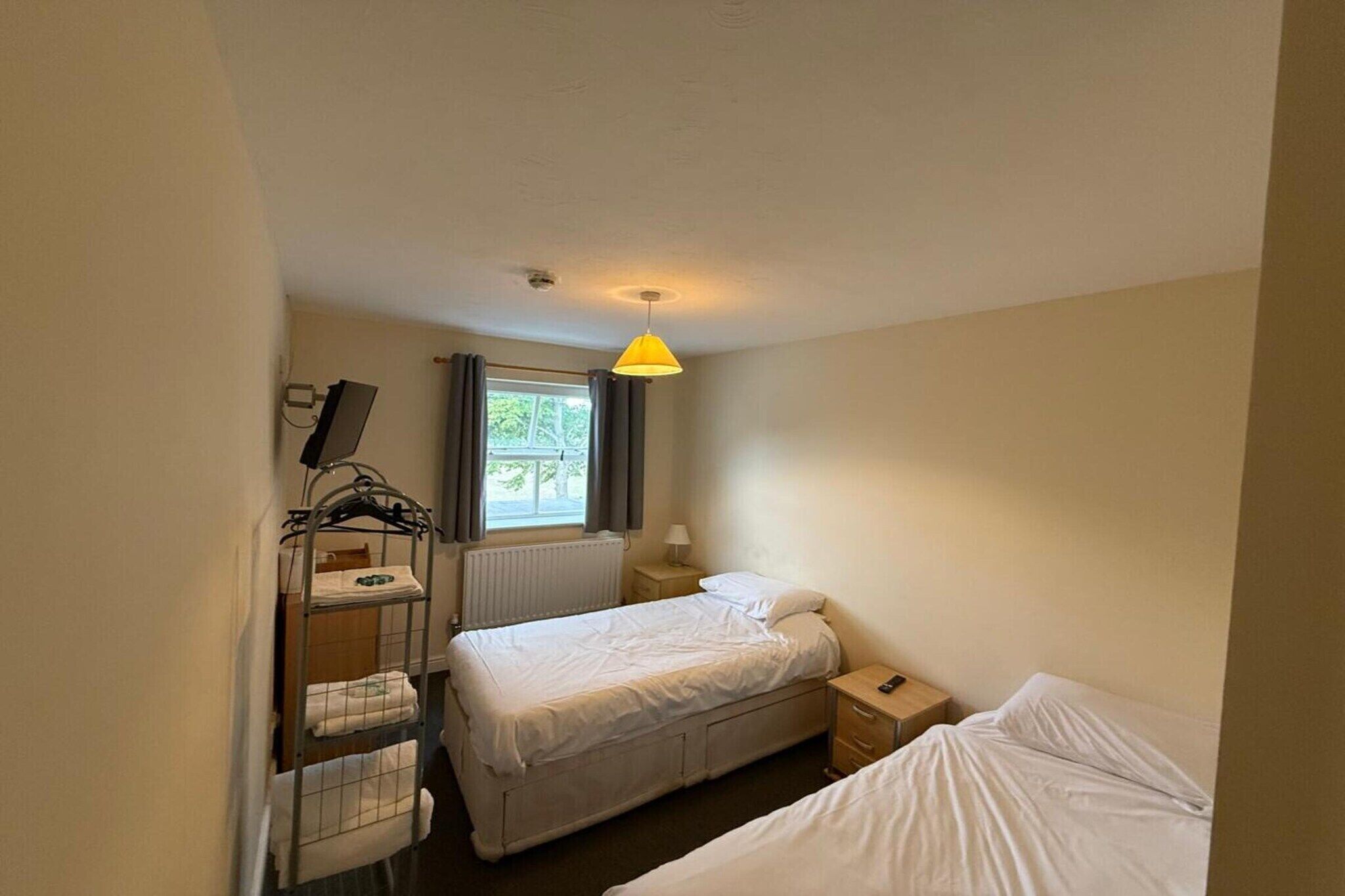 Una stanza piccola e pulita con un letto, un comodino, una lampada e una finestra con tende.