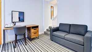 Une pièce moderne avec un tapis à rayures, un canapé gris, un bureau en bois avec une chaise et un miroir au mur.