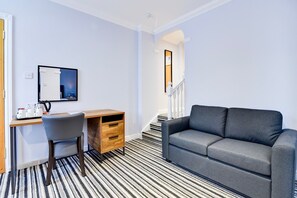 Une pièce moderne avec un tapis à rayures, un canapé gris, un bureau en bois avec une chaise et un miroir au mur.