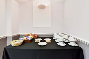 Une table de buffet avec des plateaux étiquetés pour l’eau chaude et le café, un panier de collations et une variété de produits emballés.
