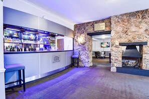 Un espace bar avec un mur en pierre et une cheminée, des tabourets de bar et un panneau indiquant les équipements de l’hôtel.