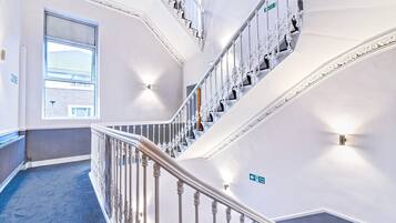 A multi-level interior with a staircase, a window with a view of a building, and a sign indicating a direction.