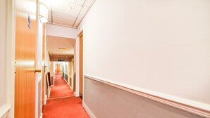 A hotel corridor with wooden doors, a red carpet, and a white wall.