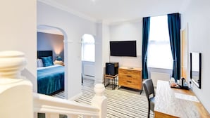 A hotel room with a bed, a desk, a TV, and a window with curtains.