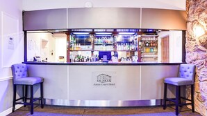 Zona de bar con pared de piedra de fondo, dos taburetes y un cartel que indica que se trata del Hotel Aston Court.