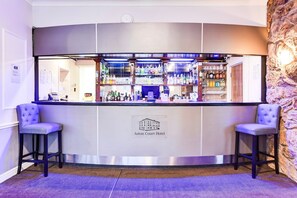 Zona de bar con pared de piedra de fondo, dos taburetes y un cartel que indica que se trata del Hotel Aston Court.