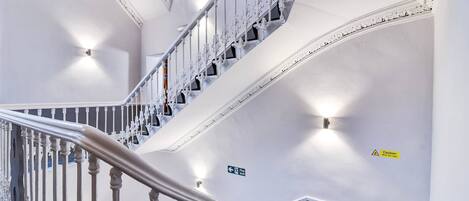 A multi-level interior with a staircase, fire exit signs, and caution tape.