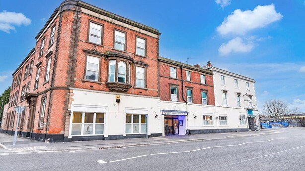 Un edificio en esquina con fachada de ladrillo y una sección blanca con un cartel que dice 'Aston Court Hotel'.