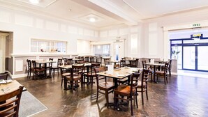 Un comedor amplio con varias mesas y sillas, una barra central y ventanas grandes que proporcionan luz natural.