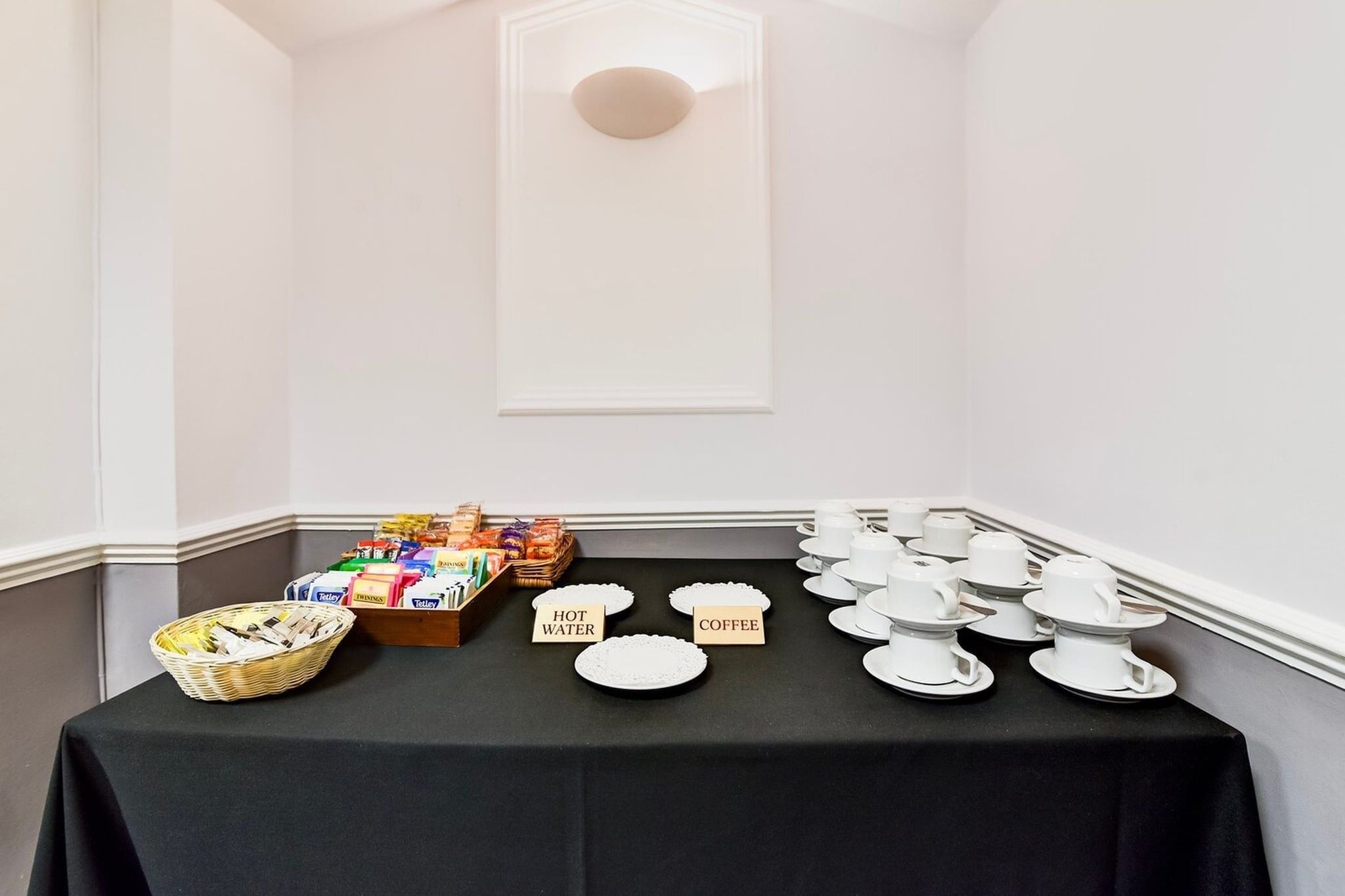 A buffet table with labeled plates for hot water and coffee, a basket of snacks, and a variety of packaged goods.
