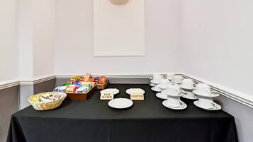 A buffet table with labeled plates for hot water and coffee, a basket of snacks, and a variety of packaged goods.