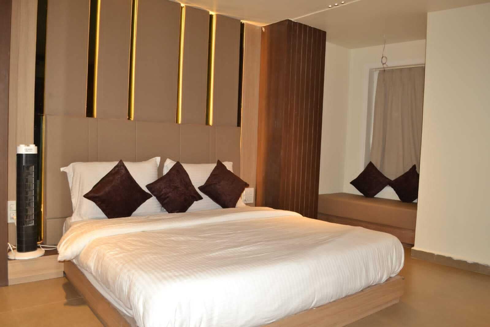 A modern hotel room with a large bed, a bedside table, a mirror, and a wall-mounted heater.