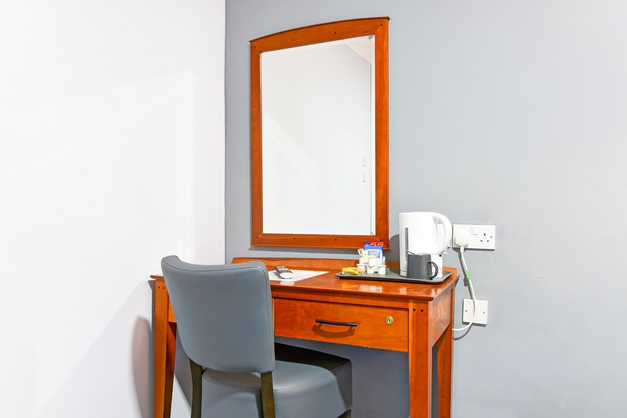 Une chambre d’hôtel avec un bureau en bois, une chaise, un miroir et une machine à café.