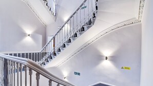 A multi-level interior with a white staircase, directional signs, and a caution sign. - Standard Family of 3 Room (Derby)