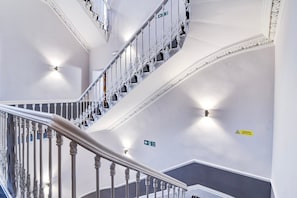 A multi-level interior with a white staircase, directional signs, and a caution sign. - Standard Family of 3 Room (Derby)