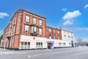 A corner building with a brick facade, a white storefront, and a sign for Aston Court Hotel. - Standard Family of 3 Room (Derby)