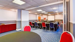 A conference room with a long table, multiple chairs, a projector screen, and a whiteboard. - Standard Family of 3 Room (Derby)