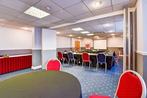 A conference room with a long table, multiple chairs, a projector screen, and a whiteboard. - Standard Family of 3 Room (Derby)