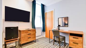 A hotel room with a flat-screen TV, wooden furniture, a desk, and a mirror.