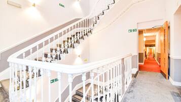 A grand staircase with white balustrades and a carpeted floor leading to a brightly lit hallway.