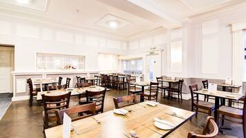 A spacious dining area with multiple tables and chairs, a white interior, and a large window providing natural light.