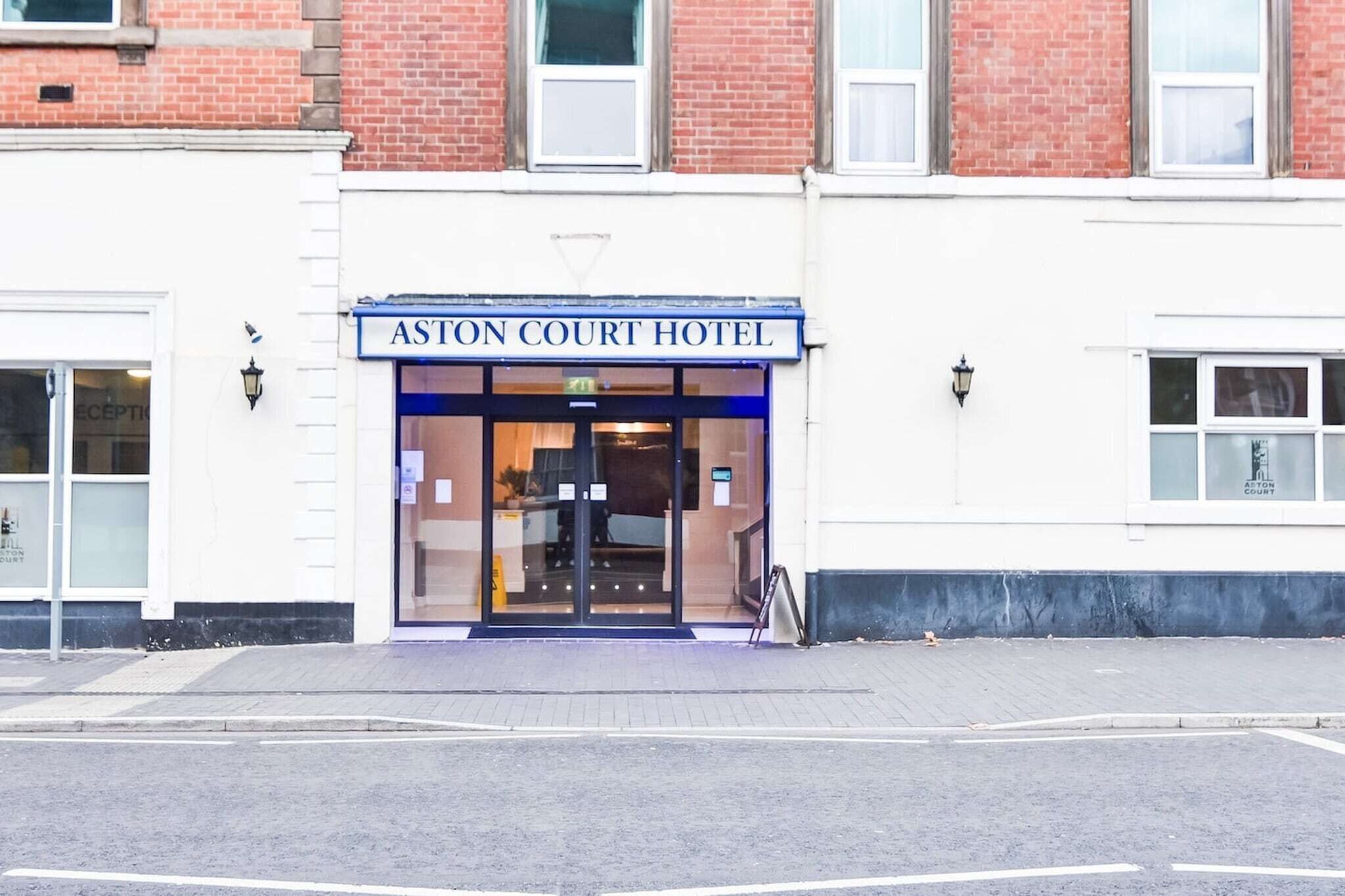 The exterior of the Aston Court Hotel with a clear entrance, a sign above the doors, and a visible reception area inside.