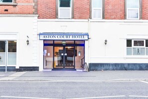 The exterior of the Aston Court Hotel with a clear entrance, a sign above the doors, and a visible reception area inside.