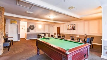 Een biljartkamer met een pooltafel, stoelen en een dartbord.