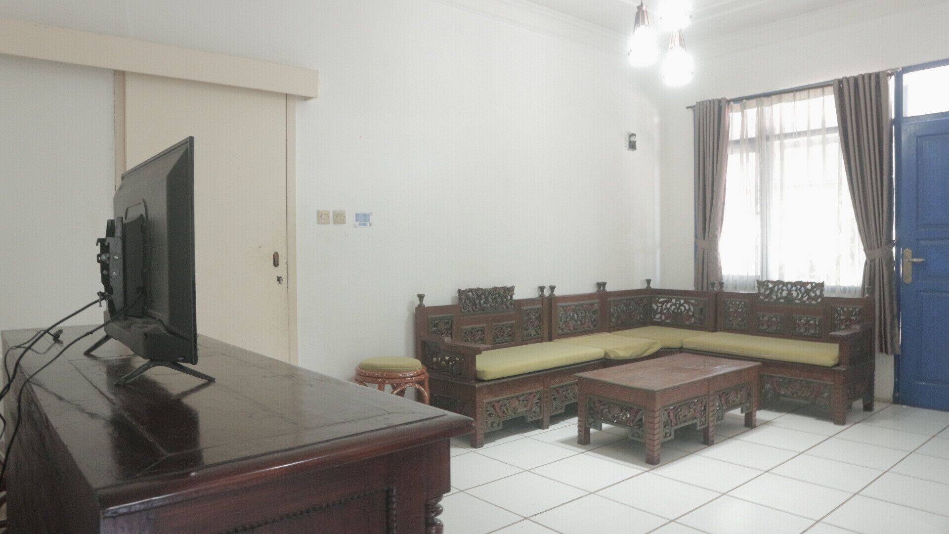 A living room with a television on a wooden table, a sofa with cushions, a small wooden stool, and a blue door.